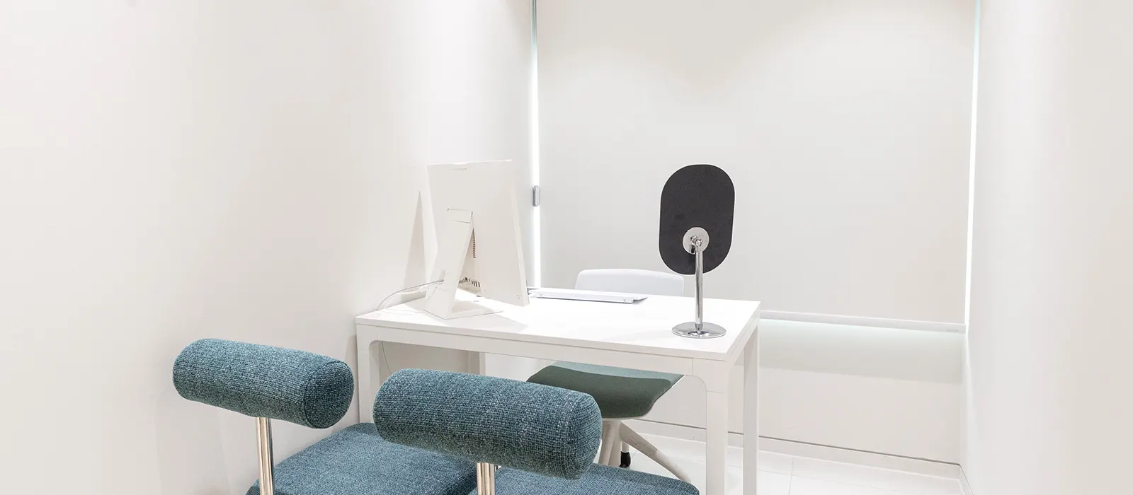 Private consultation room with a desk, mirror and teal chairs